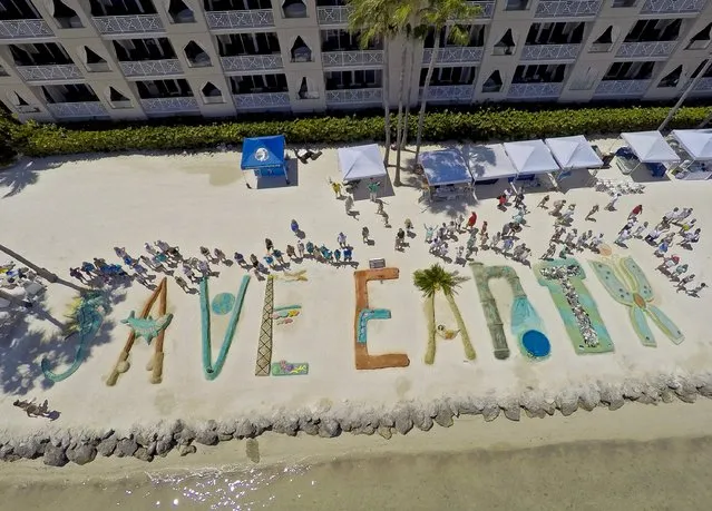 Sand sculpturists stand by their creations at the Cheeca Lodge Resort in Islamorada, Florida April 24, 2016. People gathered on the resort's beach to create sand art letters to spell out “Save Earth” during an Earth Day event in the Florida Keys. (Photo by Bob Care/Reuters/Courtesy Florida Keys News Bureau)