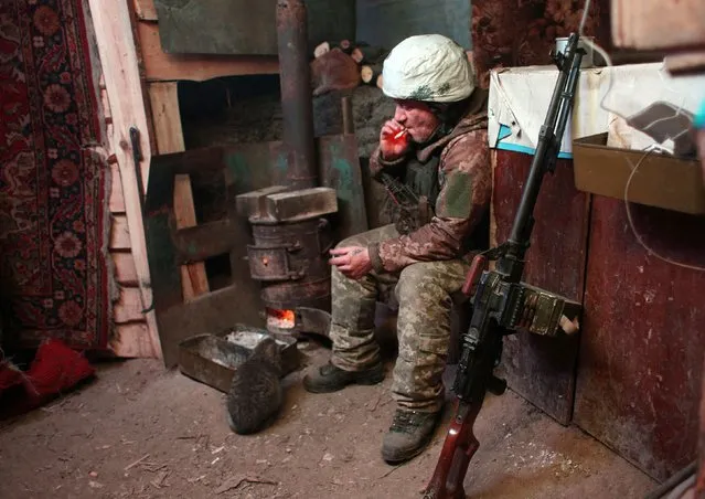 An Ukrainian Military Forces serviceman smokes in a dugout, as he and a cat sit near a wood burner on the frontline with the Russia-backed separatists near Zolote village, in the eastern Lugansk region, on January 21, 2022. Ukraine's Foreign Minister Dmytro Kuleba on January 22, 2022, slammed Germany for its refusal to supply weapons to Kyiv, urging Berlin to stop “undermining unity” and “encouraging Vladimir Putin” amid fears of a Russian invasion. (Photo by Anatolii Stepanov/AFP Photo)