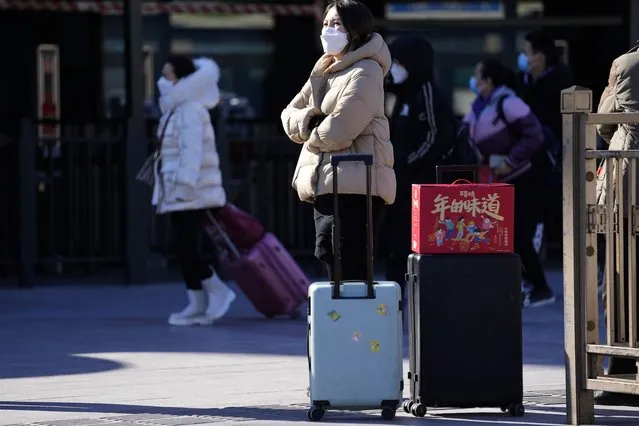 A traveler waits outside the Beijing railway station with her trolley bags and a gift box with the words “The taste of New Year” in Beijing, China, Friday, January 28, 2022. (Photo by Ng Han Guan/AP Photo)
