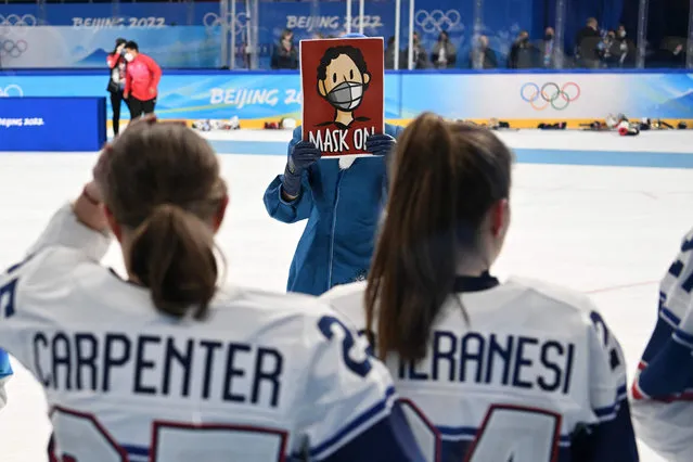 A staff of the Beijing 2022 Winter Olympic Games holds a placard reading “Mask on” as USA's players react after their defeat in the women's gold medal match of the Beijing 2022 Winter Olympic Games ice hockey competition between Canada and USA, at the Wukesong Sports Centre in Beijing on February 17, 2022. (Photo by Kirill Kudryavtsev/AFP Photo)