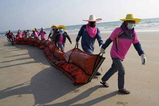 Workers drag an oil spill boom out onto Mae Ram Phueng Beach in hopes of containing any oil washing ashore from a recent spill off the coast of Rayong, eastern Thailand, Friday, January 28, 2022. An oil slick off the coast of Thailand continued to expand Friday and was approaching beaches on the east coast, home to fragile coral and seagrass, officials said. (Photo by Sakchai Lalit/AP Photo)
