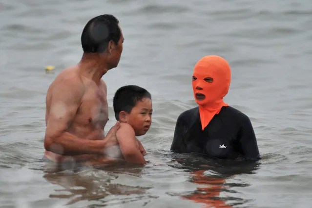 A man takes a child from a swimmer wearing a hood known as facekini near the beach in Qingdao, east China's Shandong province, China, 16 July 2015. The hood is meant to protect the swimmer's face from sun tan, sting injury of jellyfish and insolation. (Photo by Wang Haibin/EPA)