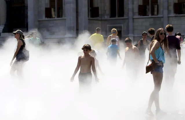 Tourists cool off in water vapor in front of the Hungarian Parliament during a hot summer day in Budapest, Hungary, July 22, 2015. (Photo by Bernadett Szabo/Reuters)
