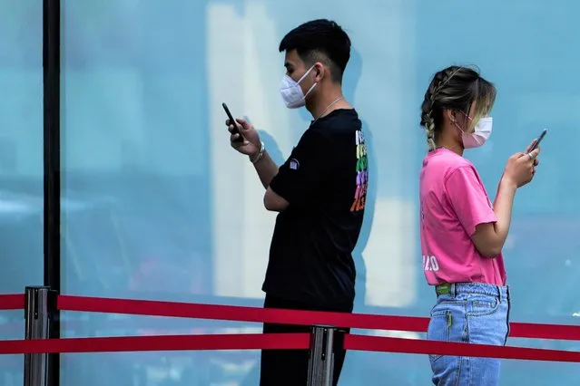 People browsing their smartphones as they wait in line for COVID testing outside a shopping mall on Sunday, May 22, 2022, in Beijing. (Photo by Andy Wong/AP Photo)