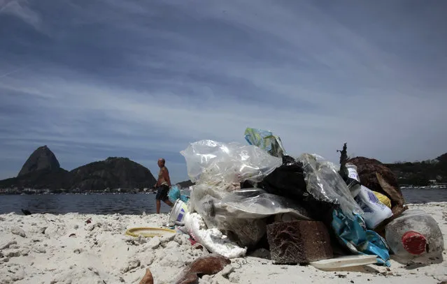 A man walks, with the Sugar Loaf Mountain in the background, near garbage on Botafogo beach in the Guanabara Bay in Rio de Janeiro March 12, 2014. (Photo by Sergio Moraes/Reuters)