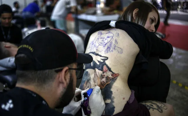 A tattoo artist makes a tattoo on the back of a young woman during the Tattoo Week in Sao Paulo, Brazil, July 14, 2017. (Photo by Miguel Schincariol/AFP Photo)