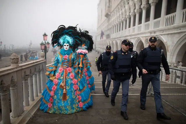 Police walk near masked and costumed people on the streets of Venice near San Marco square during the Carnival in Venice, Italy, 23 Febru​ary 2020. (Photo by Abir Sultan/EPA/EFE)