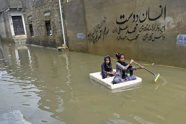 Girls use a temporary raft across a flooded street in a residential area after heavy monsoon rains in Karachi on July 26, 2022. A weather emergency was declared in Karachi as heavier-than-usual monsoon rains continue to lash Pakistan's biggest city, flooding homes and making streets impassable. (Photo by Rizwan Tabassum/AFP Photo)
