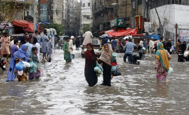 People wade through a flooded road in a business district after a heavy rainfall in Karachi, Pakistan, Saturday, July 9, 2022. Several people have died in rain-related incidents across Pakistan during the past three weeks, a top officials said. (Photo by Fareed Khan/AP Photo)