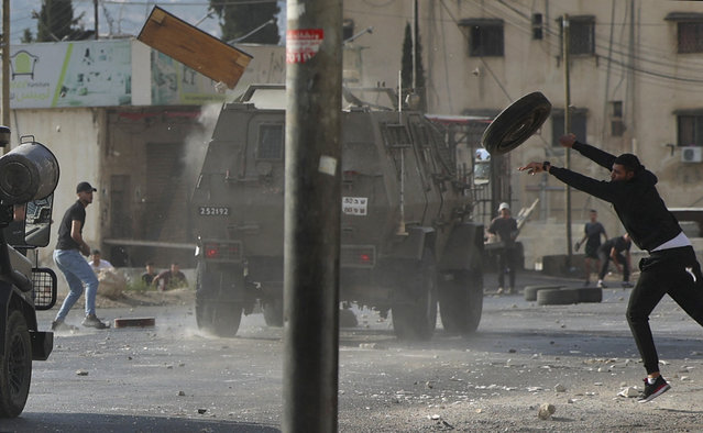 Palestinian youths throw objects at army vehicles during a military operation by the Israeli army to arrest wanted persons from the Balata camp near the West Bank city of Nablus, on August 17, 2022. (Photo by Jaafar Ashtiyeh/AFP Photo)