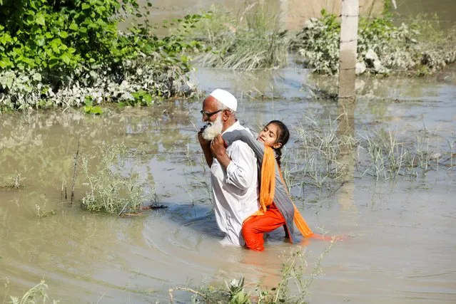 A man wades through flood waters carrying his grand daughter on his back following rains and floods during the monsoon season in Charsadda, Pakistan on August 28, 2022. (Photo by Fayaz AzizAziz/Reuters)