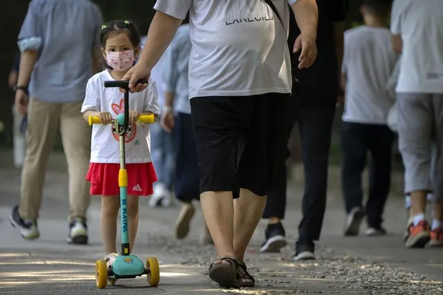 A child wearing a face mask rides a scooter along a path at a public park in Beijing, Tuesday, August 30, 2022. (Photo by Mark Schiefelbein/AP Photo)