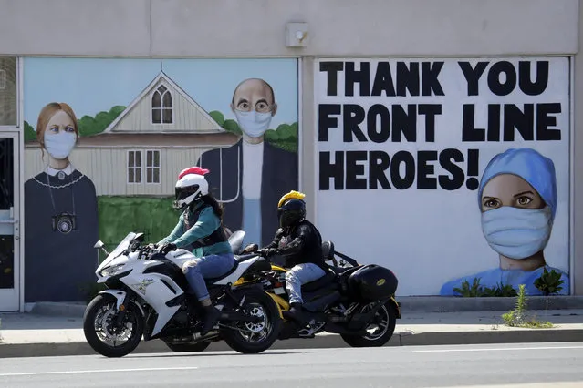 Motorcyclists go by a recently painted mural with a depiction of artist Grant Wood's famed American Gothic painting, subjects wearing masks, Thursday, April 30, 2020, in Torrance, Calif. The state of California continues a stay-at-home order amid the COVID-19 pandemic. (Photo by Marcio Jose Sanchez/AP Photo)