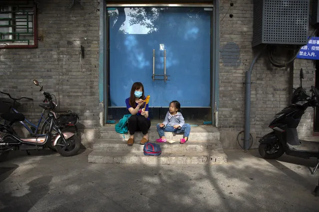 A woman wearing a face mask to protect against the spread of the new coronavirus shares a snack with a girl as they sit on a pedestrian shopping street in Beijing, Saturday, May 16, 2020. (Photo by Mark Schiefelbein/AP Photo)