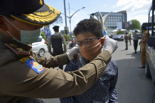 A municipal officer adjusts the face mask of a motorist after he was stopped by municipal authorities for not wearing the item amid  the COVID-19 coronavirus pandemic in Banda Aceh on May 18, 2020. (Photo by Chaideer Mahyuddin/AFP Photo)