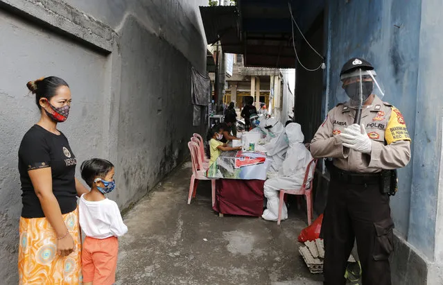A police officer wearing a face shield and a face mask talks to residents during a coronavirus antibody test from health workers in Bali, Indonesia, Wednesday, May 27, 2020. (Photo by Firdia Lisnawati/AP Photo)