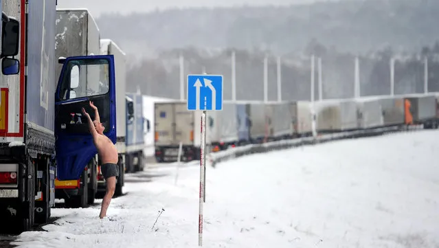 A driver of a trailer truck does his morning exercises as his truck stands in line at the Belarusian-Lithuanian border near the Kamienny Log border point, some 150 km northwest of Minsk, on February 14, 2016. About a hundred Russian trucks wait at the border due to a new road tax imposed on Russian long distance truckers. (Photo by Sergei Gapon/AFP Photo)