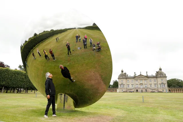British-Indian artist Anish Kapoor is reflected in one of his sculptures as he poses for photographs in the gardens at Houghton Hall in Norfolk, Britain on July 9, 2020. (Photo by Matthew Childs/Reuters)