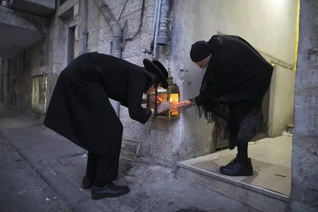 An ultra-Orthodox Jewish man and woman light candles on the second night of the Jewish holiday of Hanukkah, in the Ultra-Orthodox neighbourhood of Mea Shearim of Jerusalem, on December 13, 2017. The holiday commemorates the re-dedication of the holy temple in Jerusalem after the Jews' 165 B.C. victory over the Hellenist Syrians when Antiochus, the Greek King of Syria, outlawed Jewish rituals and ordered the Jews to worship Greek gods. (Photo by Menahem Kahana/AFP Photo)