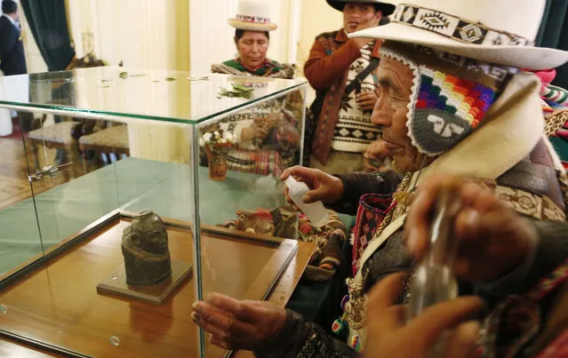 Indigenous Andean spiritual counselors known as Amautas spray alcohol on the case protecting a pre-Columbian relic made of carved stone during its presentation at the presidential palace after it was returned from Switzerland, in La Paz, Bolivia, Monday, November 17, 2014. Bolivia recovered the 2000 year old relic after it had been in Switzerland for 156 years. According to experts, it's a woman representing an Ekeko Andean deity, god of fertility and abundance, from the Pucara culture that inhabited the Lake Titicaca region. (Photo by Juan Karita/AP Photo)