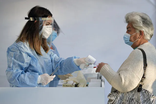 An electoral staff member checks the temperature of a woman, wearing a face mask for protection against the COVID-19 infection, before allowing her in a voting station in Bucharest, Romania, Sunday, September 27, 2020. Some 19 million registered voters are choosing local officials, council presidents and mayors to fill more than 43,000 positions across the European Union nation. (Photo by Vadim Ghirda/AP Photo)