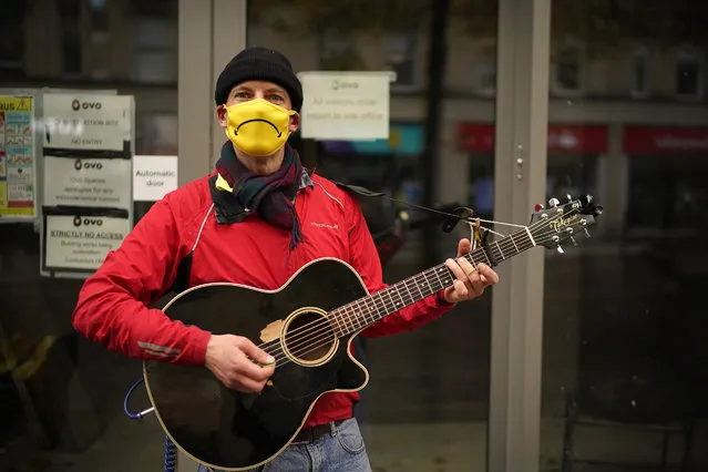 Busker Tony Black turns his “smiley” face mask upside down to reflect the current mood as he entertains shoppers on October 22, 2020 in Sheffield, England. The county of South Yorkshire, which includes the city of Sheffield will move to Tier 3 “Very High” Covid-19 alert on Saturday. (Photo by Christopher Furlong/Getty Images)