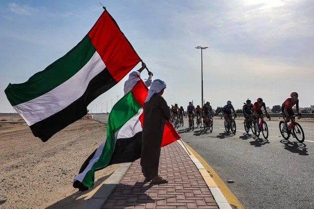 People stand with Emirati flags as the peloton rides past during the first stage of the UAE cycling tour from al-Dhafra Castle to Qassar al-Mighayra St in al-Mirfa in the emirate of Abu Dhabi on February 20, 2023. (Photo by Giuseppe Cacace/AFP Photo)
