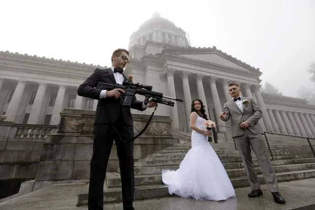 The best man in a wedding party, who all declined to be identified, holds an AR-10 rifle he was handed while the party was having their pre-wedding portraits taken on the steps of the capitol before a rally nearby by gun-rights advocates to protest a new expanded gun background check law in Washington state Saturday, December 13, 2014, in Olympia, Wash. (Photo by Elaine Thompson/AP Photo)
