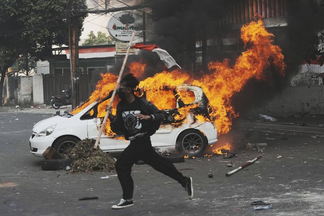 A protester runs past a burning car during a protest following the death of a delivery rider in clashes between riot police and students protesting against lawmakers' allowances, in Jakarta, Indonesia, Friday,August 29, 2025. (Photo by Tatan Syuflana/AP Photo)