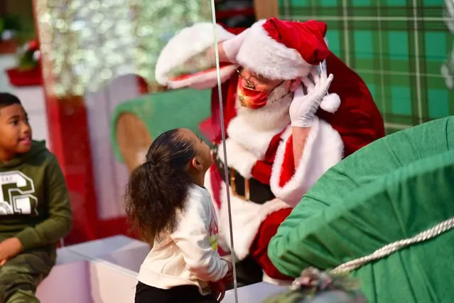 Brother and sister DeShaye, 8, and Shaye'Lah Powell, 4, speak to a man dressed as Santa Claus, who sits behind a plexiglass divider due to the coronavirus at the Willow Grove Park Mall in Willow Grove, Pennsylvania, November 14, 2020. (Photo by Mark Makela/Reuters)