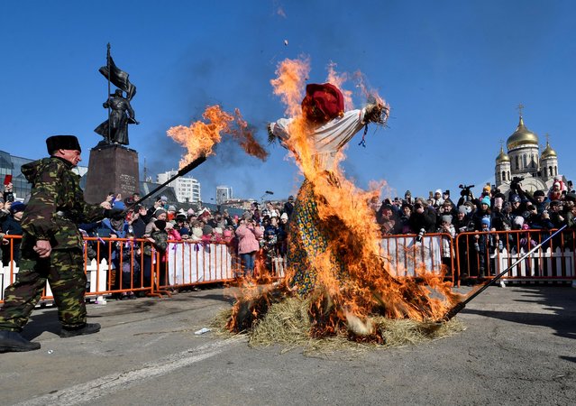 Spectators gather around a burning effigy of Lady Maslenitsa during the celebration of Maslenitsa, also known as Pancake Week, which is a pagan holiday marking the end of winter in front of a monument of a revolutionary soldier in Russia's far eastern city of Vladivostok, Russia on March 14, 2021. (Photo by Yuri Maltsev/Reuters)