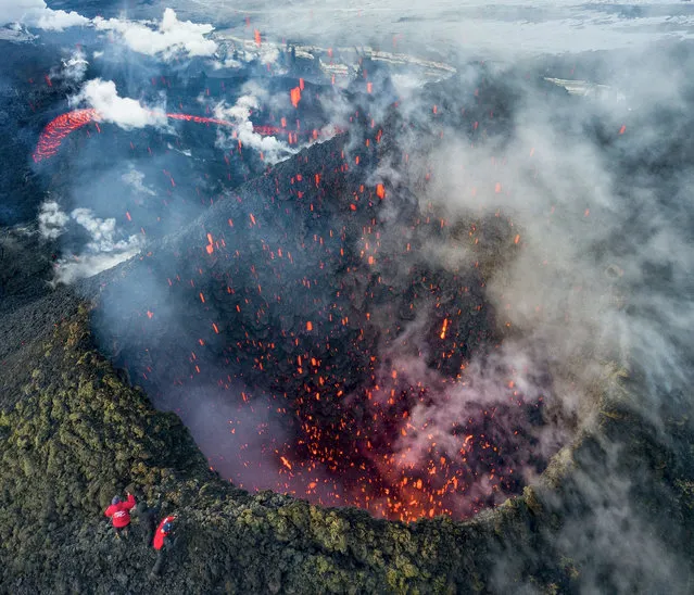 A picture taken with a drone on March 16, 2021 shows members of a local search and rescue squad taking pictures of Klyuchevskoy volcano eruption on Russia's far eastern Kamchatka peninsula. The eruption of a volcano on a Russian peninsula has attracted thrill-seeking tourists risking their lives for picturesque photos, prompting concerns in recent days from local emergency responders. (Photo by Maxim Fesyunov/AFP Photo)