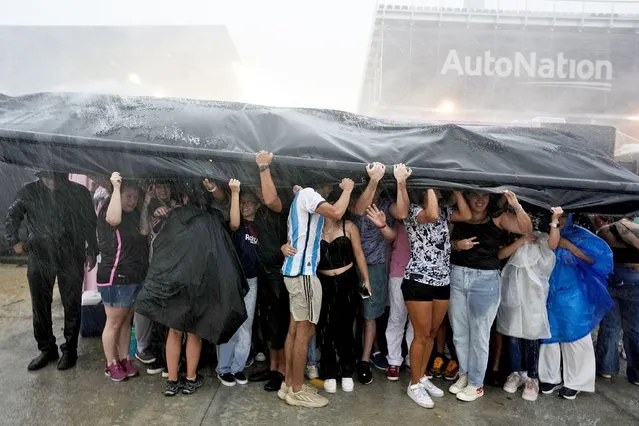 Fans seek shelter from a torrential downpour as they wait to enter DRV Pink Stadium, home of the Inter Miami MLS soccer team, for an event to present international superstar Lionel Messi one day after the team finalized his signing through the 2025 season, Sunday, July 16, 2023, in Fort Lauderdale, Fla. (Photo by Rebecca Blackwell/AP Photo)
