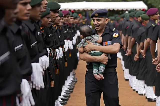 An Indian Army soldier carrying his baby reacts as he walks past graduating soldiers from the first batch of Agniveer scheme during their graduation ceremony in Bengaluru, India, Friday, August 4, 2023. Agniveer, a new short-term job program announced by the government for the military was launched in June 2022. Seventy-five percent of the recruits will be compulsorily retired after four years with no pension benefits. (Photo by Aijaz Rahi/AP Photo)