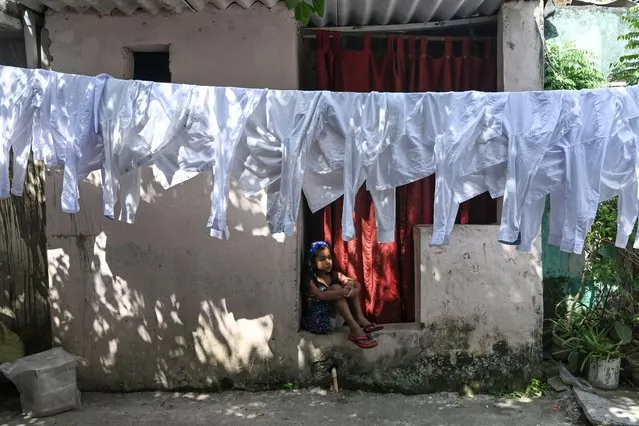 A girl sits next to a line with washed shirts drying at an open air laundry in New Delhi on September 28, 2023. (Photo by Arun Sankar/AFP Photo)