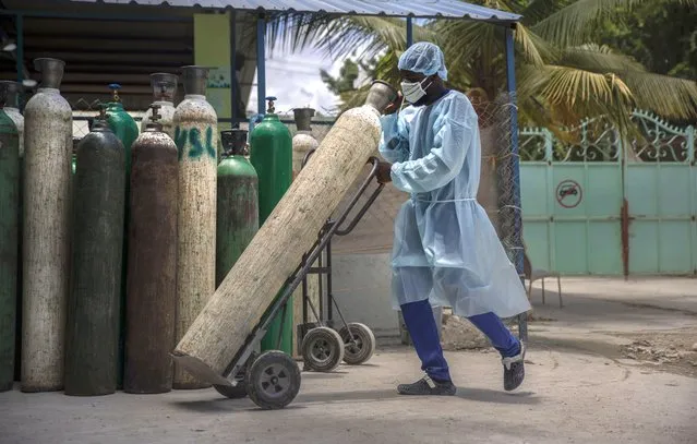 A hospital emplyee wearing protective gear as a precaution against the spread of the new coronavirus, transports oxygen tanks, in Port-au-Prince, Haiti, Saturday, June 5, 2021. (Photo by Joseph Odelyn/AP Photo)