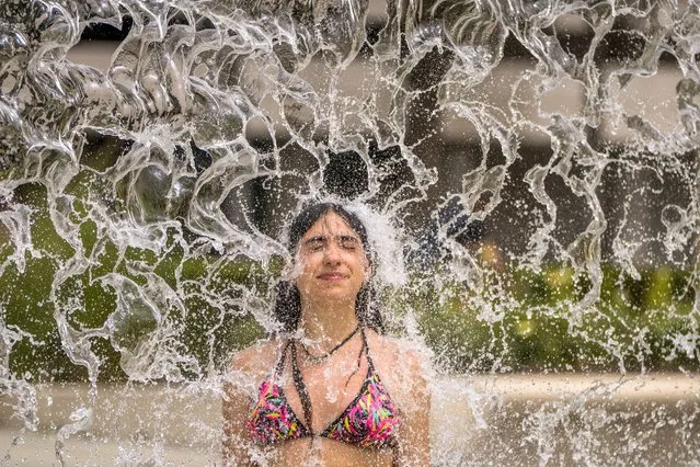 A woman cools off in a fountain in Cordoba, southern Spain, Sunday, July 11, 2021. Spain is suffering a weekend of record-breaking high temperatures, with the thermometer set to top 44 Celsius (111 Fahrenheit) in some areas. (Photo by Manu Fernandez/AP Photo)