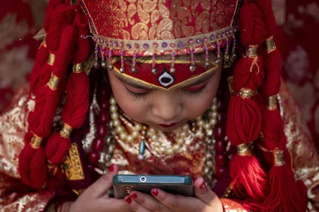 A young girl dressed as living goddess Kumari checks a mobile phone as she waits for Kumari Puja, a worship ritual at Hanuman Dhoka, Basantapur Durbar Square, Kathmandu, Nepal, Wednesday, September 27, 2023. (Photo by Niranjan Shrestha/AP Photo)