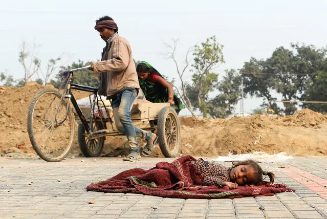 Indian labourers work at a construction site pulling a tricycle while a chid sleeps on a blanket nearby in New Delhi on January 13, 2019. (Photo by Sajjad Hussain/AFP Photo)