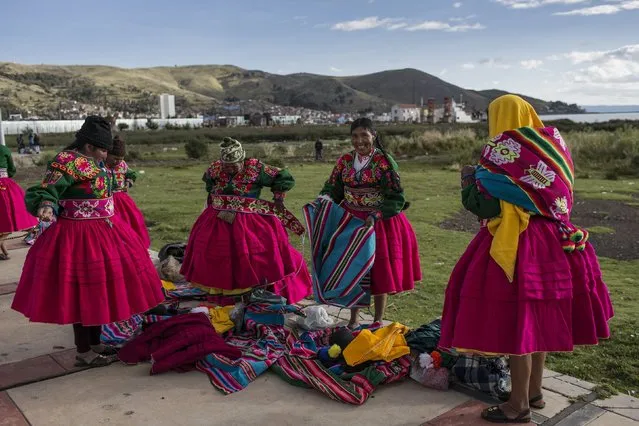 In this January 29, 2017 photo, dancers put on their costumes near the shore of Lake Titicaca prior to their performance for Virgin of Candelaria celebrations in Puno, Peru. Some competing groups wear shoes made with alpaca skin, collars hung with ears of corn and hats adorned with old coins or the bright-colored feathers of Amazonian birds. (Photo by Rodrigo Abd/AP Photo)