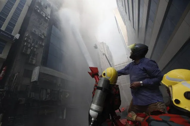 A commuter watches firefighters work to douse a fire in a multi-storied office building in Dhaka, Bangladesh, Thursday, March 28, 2019. A fire in a high-rise office building in Bangladesh's capital on Thursday killed seven people and injured dozens more, police said. (Photo by Mahmud Hossain Opu/AP Photo)