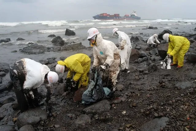 This picture taken on March 25, 2016 shows workers removing oil from the beach, leaked from the damaged Taiwanese cargoship T. S. Lines co. (background) grounded offshore near Shihmen district in New Taipei City. The ongoing operation to remove oil leaking from a ship belonging to Taiwan's TS Lines Co., which ran aground on a shallow reef offshore earlier this month has been hampered by bad weather. (Photo by Sam Yeh/AFP Photo)