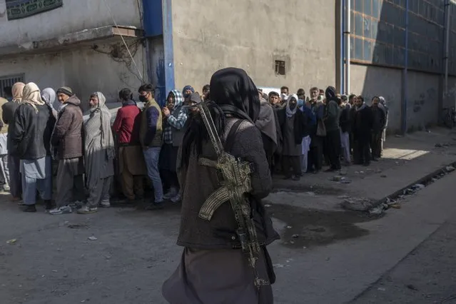 A Taliban fighter secures the area as people queue to receive cash at a money distribution site organized by the World Food Program (WFP) in Kabul, Afghanistan, Wednesday, November 17, 2021. (Photo by Petros Giannakouris/AP Photo)