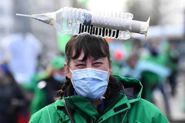 A health care worker carries a symbolic syringe shaped item on her head as she participates in a trade union demonstration against their mandatory anti-Covid 19 vaccination, as part of a major day of action, in Brussels on December 7, 2021. (Photo by John Thys/AFP Photo)