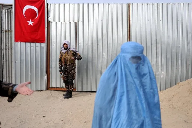 A Taliban fighter is seen as a woman arrives to receive a package being distributed by a Turkish humanitarian aid group at a distribution centre in Kabul, Afghanistan, December 15, 2021. (Photo by Ali Khara/Reuters)