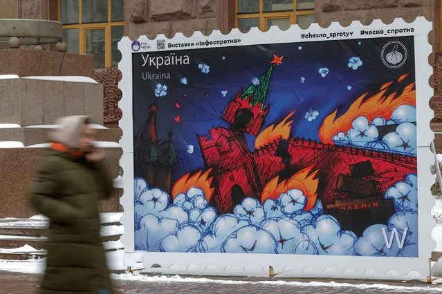 A woman walks past a giant mock-up of a postal stamp depicting a burning Moscow Kremlin, amid Russia's attack on Ukraine, in Kyiv, Ukraine on January 12, 2023. (Photo by Valentyn Ogirenko/Reuters)