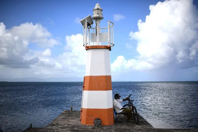 A man sits against a light-house with his bicycle in Petit-Canal on the French Caribbean island of Guadeloupe on December 16, 2021. (Photo by Christophe Archambault/AFP Photo)