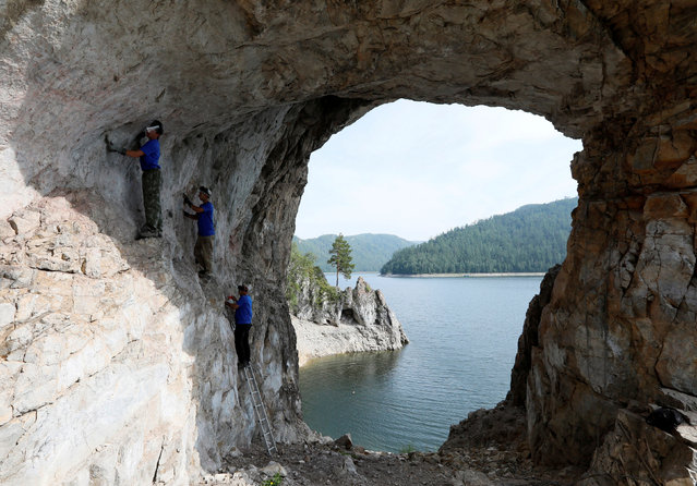 Vladimir Volkov, Denis Yakovlev and Igor Volkov, members of the amateur rock-climbing community “Stolbists”, or Stolby goers, clean the surface of the Tsarskiye Vorota (Tsar's Gate) Rock on the bank of the Biryusa River while taking part in an ecological project in the Stolby national nature reserve in the Siberian Taiga area outside Krasnoyarsk, Russia on July 30, 2019. (Photo by Ilya Naymushin/Reuters)
