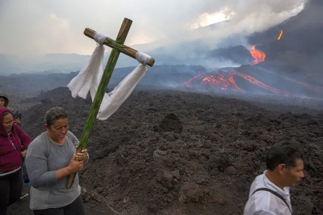 A woman carries a cross during a pilgrimage to pray that the Pacaya volcano decreases its activity in San Vicente Pacaya, Guatemala, Wednesday, May 5, 2021. The volcano, just south of the capital, has been active since early February. (Photo by Moises Castillo/AP Photo)
