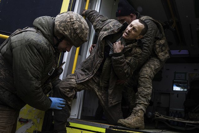 Ukrainian military medics help their wounded comrade to get out from an ambulance after arriving from the battlefield to the field hospital near Bakhmut, Ukraine, Sunday, February 26, 2023. (Photo by Evgeniy Maloletka/AP Photo)